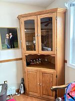 Full view of tall oak corner cabinet showing glass upper doors, open shelf, lower doors, crown moulding