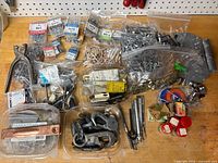 Overview of entire lot on workbench showing packaged screws, rivets, hinges, eyelets, grommet tool, saw blades and other loose hardware