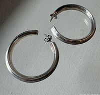 Two sterling silver hoop earrings on flat surface