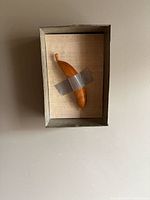 Front view of aluminum shadow box displaying taped wooden banana