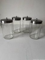 Four MGW Inc. glass jars with lids grouped