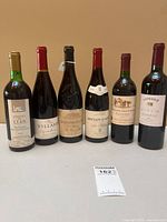 Front view of six red wine bottles lined up on table showing labels