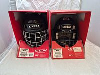 Front view of both CCM helmets in boxes showing cages and branding