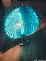 Lamp illuminated showing blue plastic slatted globe and metal base