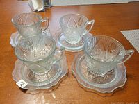 Four clear glass tea cups with matching saucers displayed on table