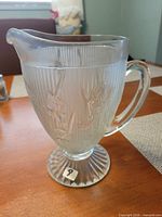 Left side view of clear pressed glass pitcher with iris pattern, showing handle and foot