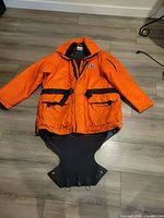 Front view of orange Mustang Survival immersion jacket with detachable black neoprene skirt attached