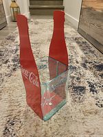 Angled view showing clear glass body and red metal bottle silhouette sides