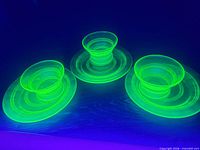 Three uranium glass bowl-and-saucer sets glowing under blacklight