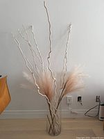 Full view of glass vase with branches and feathers against wall