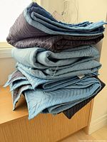 Stack of five folded light blue and navy quilted moving blankets