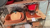Shelf showing terracotta dishes, wooden boards, red fondue set on stand