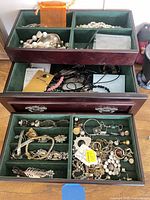 Open jewelry box showing multiple compartments filled with assorted necklaces, bracelets, earrings, brooches, rings