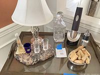 Overall lot view on tray table showing lamp, granite base with shot glasses, crystal decanter, electric wine opener, mini grinder, bowl of corks