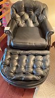 Front view of black leather tufted club chair with ottoman
