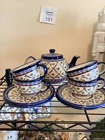 Full view of teapot, four cups and four saucers on shelf