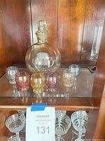 Decanter with stopper and six colored cordial glasses displayed in cabinet