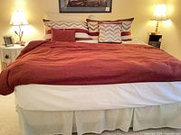 Full view of bed with burgundy duvet, chevron shams, decorative pillows, bed skirt