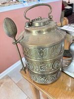 Brass tiffin carrier with spoon attached, showing etched patterns
