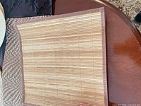 Rectangular bamboo slat placemat with brown trim on table, other placemats partially visible