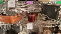 Shelf view showing copper roasting pan with inserts, red ceramic pot, black saucepan/mixing bowl