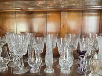 Shelf view showing variety of cut crystal stemware, two bud vases, amethyst vase and silver-topped shaker