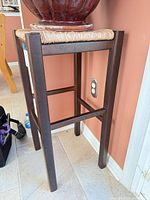 Full view of plant stand stool showing wood legs and wicker seat