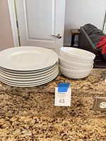 Stack of eight white dinner plates beside three white bowls on countertop