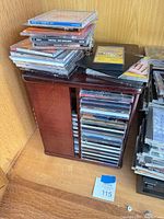 Wood CD rack filled with jewel-case CDs, additional CD stacks on top