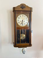 Front view of wood wall clock showing dial and glass door with pendulum visible