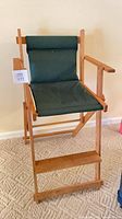 Full view of folding director's chair showing wood frame, green canvas seat/back, footrest