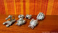 Six unpainted metal Ork Battlefortress vehicles on wood surface