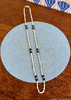 Full view of pearl and black bead necklace laid flat showing bead pattern and clasp