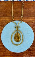Full view of brass necklace showing chain and pendant against wood background