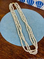 Entire triple strand pearl necklace laid flat showing overall design and clasp