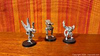 Front view of three unpainted metal miniatures on bases