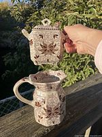 Front view of lidded sugar bowl held above matching creamer pitcher, showing overall pattern and form