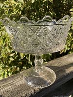 Full view of clear pressed glass pedestal compote on wood rail