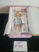 Doll in opened box showing accessories, stand and paperwork
