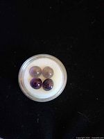 Top view of all four amethyst cabochons in display jar against black background