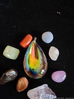 Group shot of 8 stones arranged around iridescent teardrop crystal pendant on black background