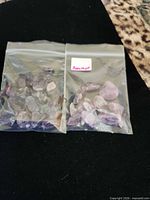 Two bags of amethyst stones side by side on black surface