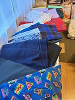 Row of folded fabrics showing navy, royal blue, plaid, floral, novelty and red floral pieces