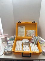 Open yellow case showing contents: peg racks, paint tubes, paperwork