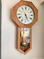 Full view of oak veneer wall clock showing octagonal dial section and glass pendulum section