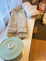 Overview of lace fabric bolt, jersey bolt, and mint satin ribbon roll on table