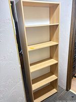 Full frontal view of tall light oak laminate bookcase with five shelves