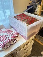 Stacked fabrics in plastic tote and folded purple floral yardage
