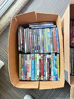 Box of assorted DVD movies—family titles visible