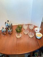 Full lot showing stainless teapot, sugar, creamer, green and clear glass cups, ceramic mugs